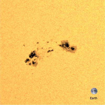 A solar active region as seen by the Helioseismic and Magnetic Imager on board the NASA Solar Dynamics Observatory. The dark circular regions are sunspots; these regions of strong magnetic field are dark as they are cool. The image of Earth is shown for scale.